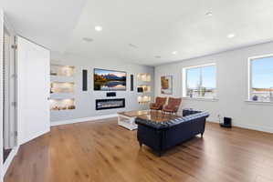 Living room featuring built in features, a glass covered fireplace, light wood-type flooring, and recessed lighting