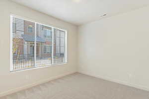 Spacious room featuring a large window with horizontal blinds, light-toned carpeting, neutral wall paint, white trim, and a ceiling-mounted air vent