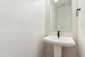 Pedestal sink featuring a black faucet, rectangular mirror, and recessed lighting
