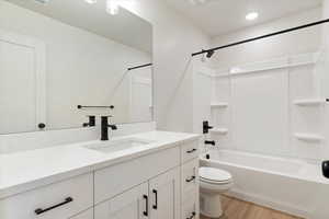 Bright white bathroom featuring a vanity with a white countertop and integrated sink, matte black fixtures, recessed lighting, and wood-finish flooring