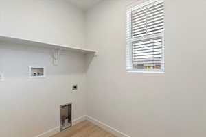Dedicated laundry space featuring a window with horizontal blinds, wood-finish flooring, a wall-mounted shelf, and appliance hookups