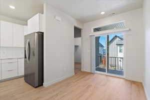 Open-concept living area featuring light wood-finish flooring and a kitchen with white cabinetry, subway tile backsplash, and a stainless steel refrigerator