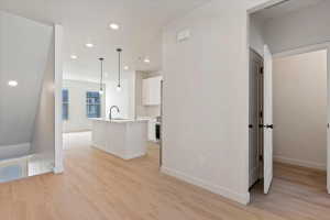 Open-concept kitchen and living area featuring light wood-finish flooring, recessed lighting, and a kitchen island with an undermount sink