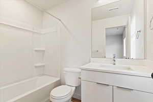 Bright bathroom featuring a white tub/shower combination, a white toilet, and a vanity with a white countertop, an integrated rectangular sink, and chrome-finish hardware