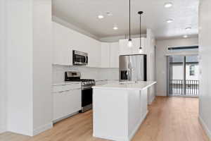 Modern kitchen featuring white cabinetry, stainless steel appliances, a subway tile backsplash, and light wood-finish flooring