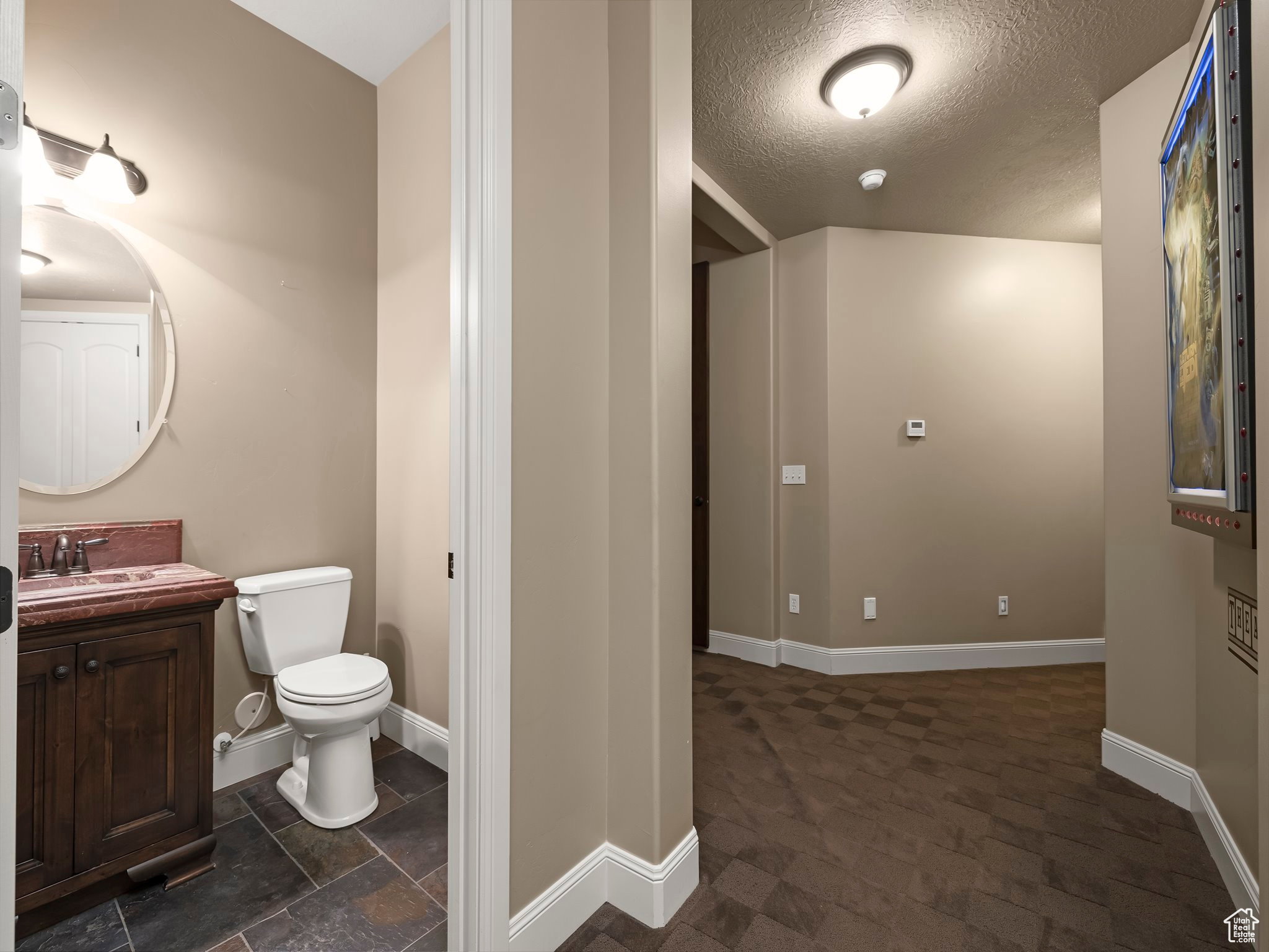 Powder room featuring a dark wood-finish vanity with a red-hued countertop, oval mirror, and slate-finish floor tiles