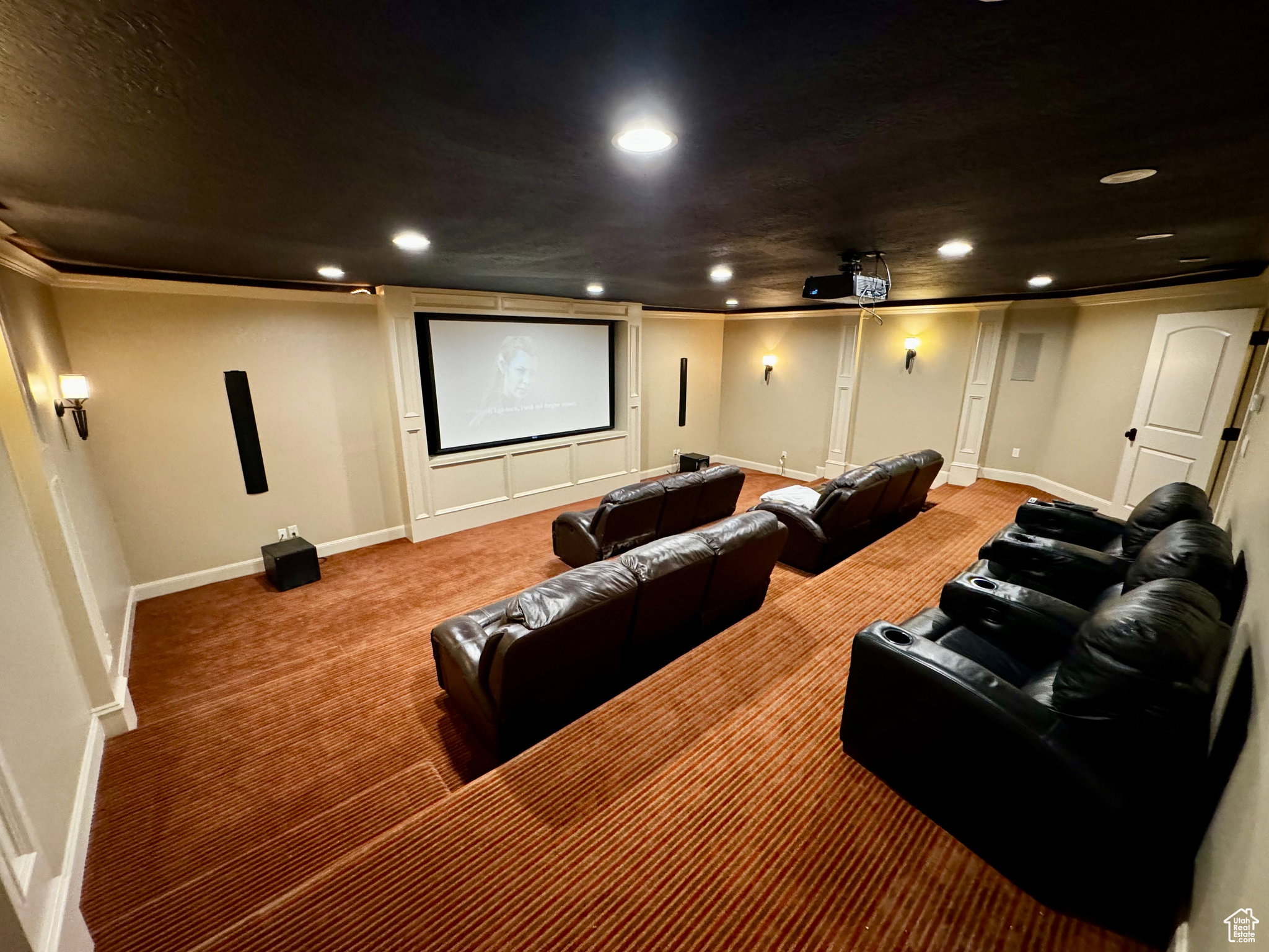 Dedicated home theater featuring a large projection screen, recessed lighting, wall sconces, and multi-tiered seating