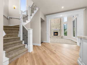 Expansive entryway featuring wood-finish flooring, a grand staircase with carpeted treads and wrought iron balusters, and a decorative sconce