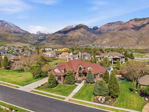 Stately property featuring a multi-gabled roofline, stone and brick facade, and a paved driveway leading to a three-car garage
