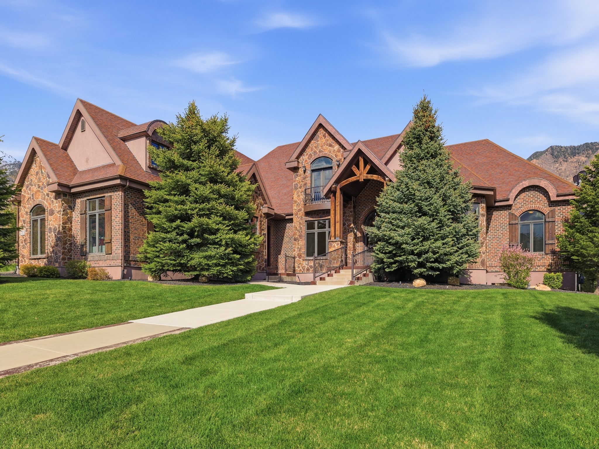 Stately brick and stone facade residence featuring a prominent gabled roofline, arched windows with decorative shutters, a covered entry with wood beam accents, and a paved walkway