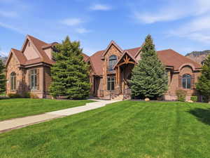 Stately brick and stone facade residence featuring a prominent gabled roofline, arched windows with decorative shutters, a covered entry with wood beam accents, and a paved walkway