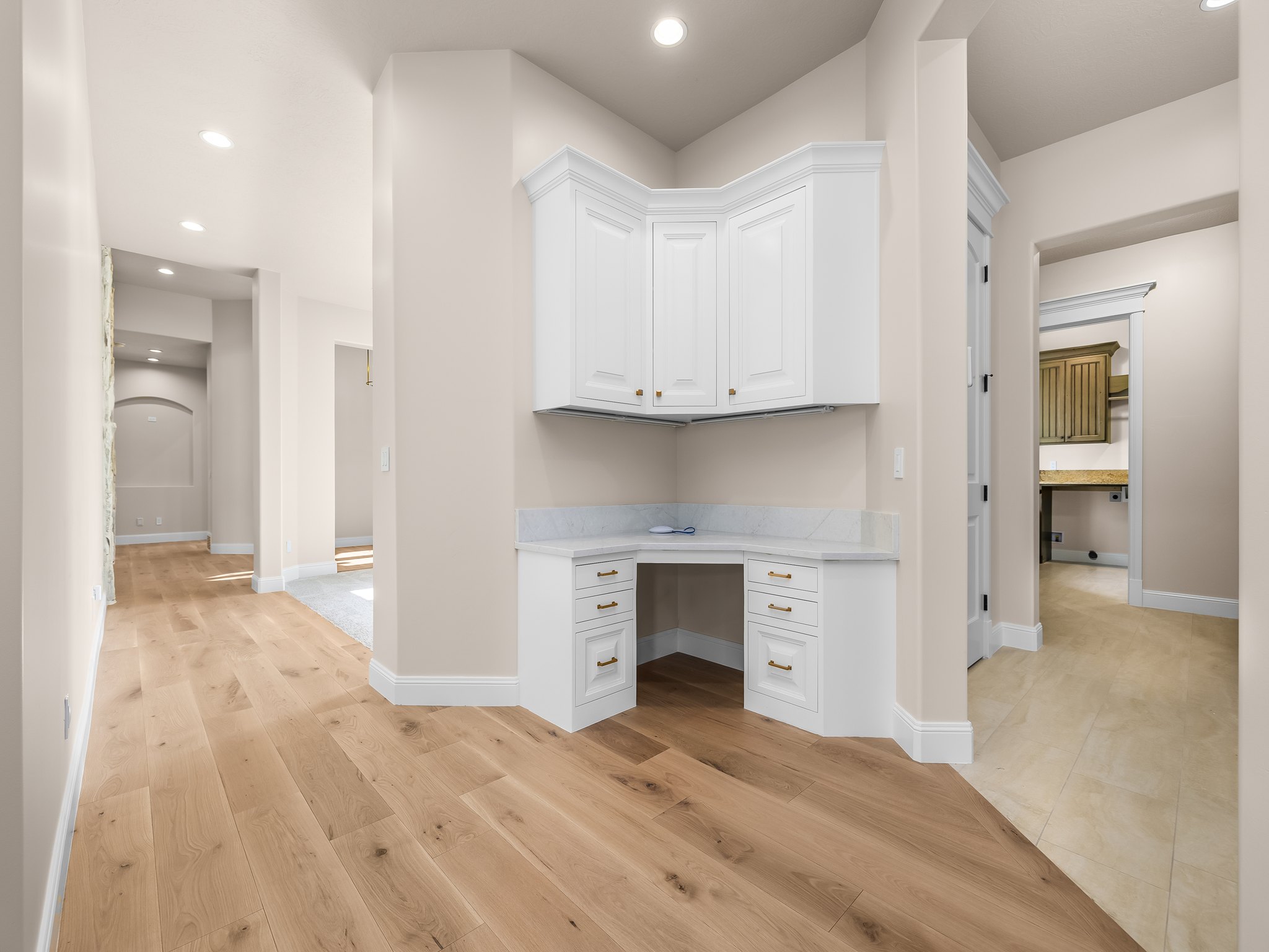 Built-in corner desk featuring white cabinetry, gold-finish hardware, and a light-toned countertop