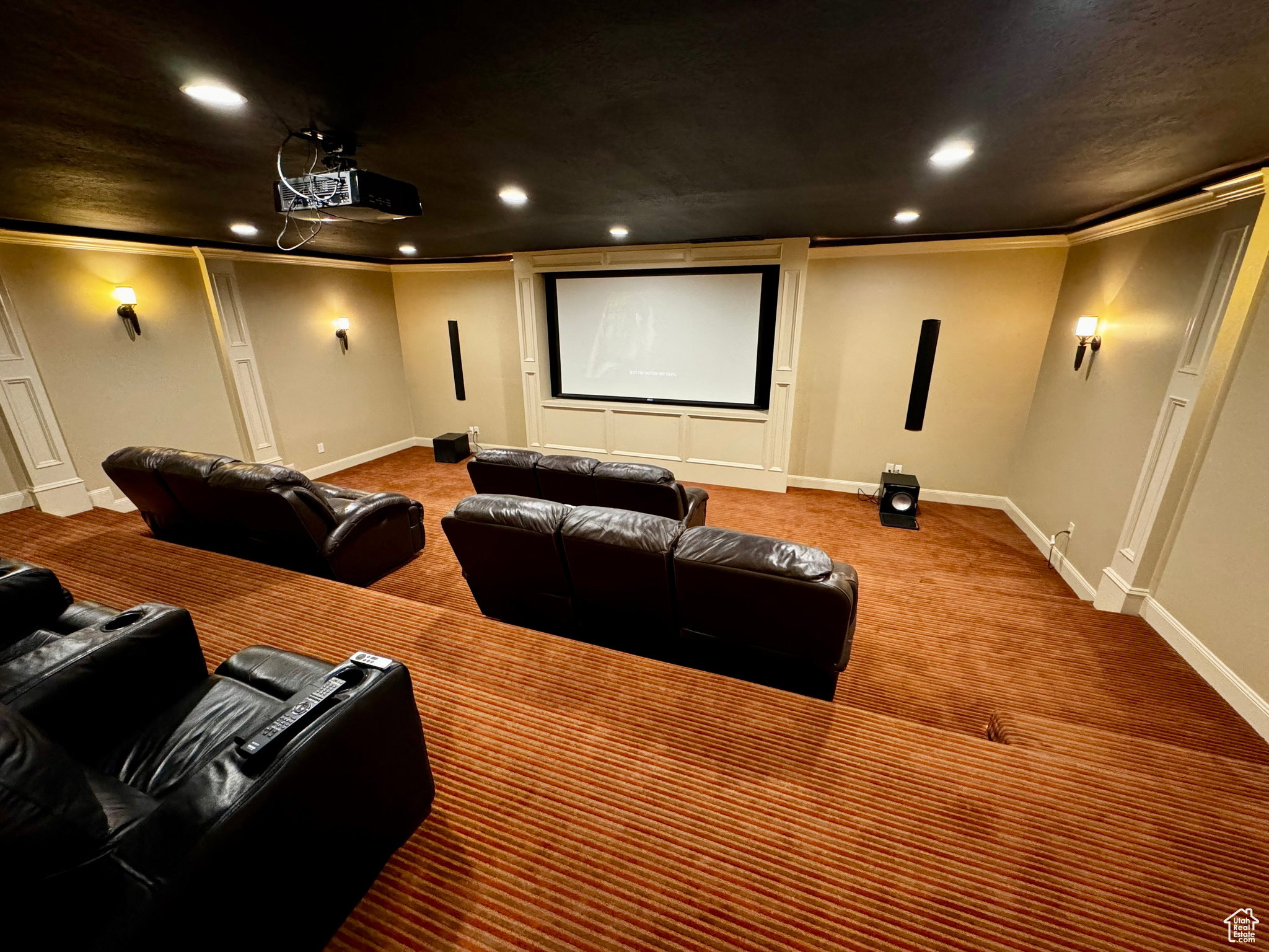 Dedicated media room featuring tiered seating, a large projection screen, built-in recessed lighting, decorative wall sconces, and a ceiling-mounted projector