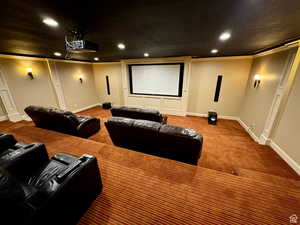 Dedicated media room featuring tiered seating, a large projection screen, built-in recessed lighting, decorative wall sconces, and a ceiling-mounted projector