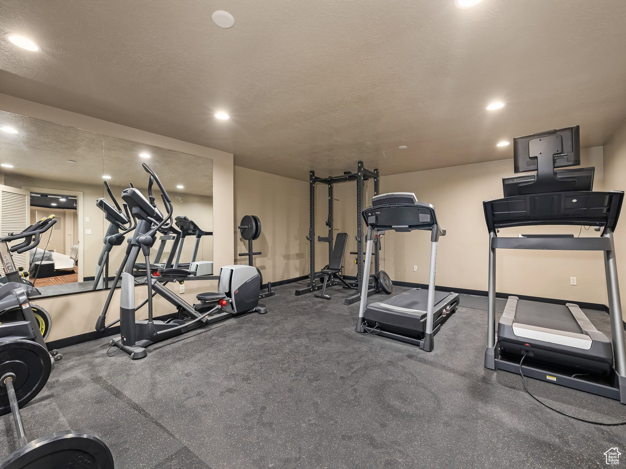 Dedicated fitness space featuring resilient black flooring, a full-wall mirror, recessed ceiling lighting, and neutral wall tones