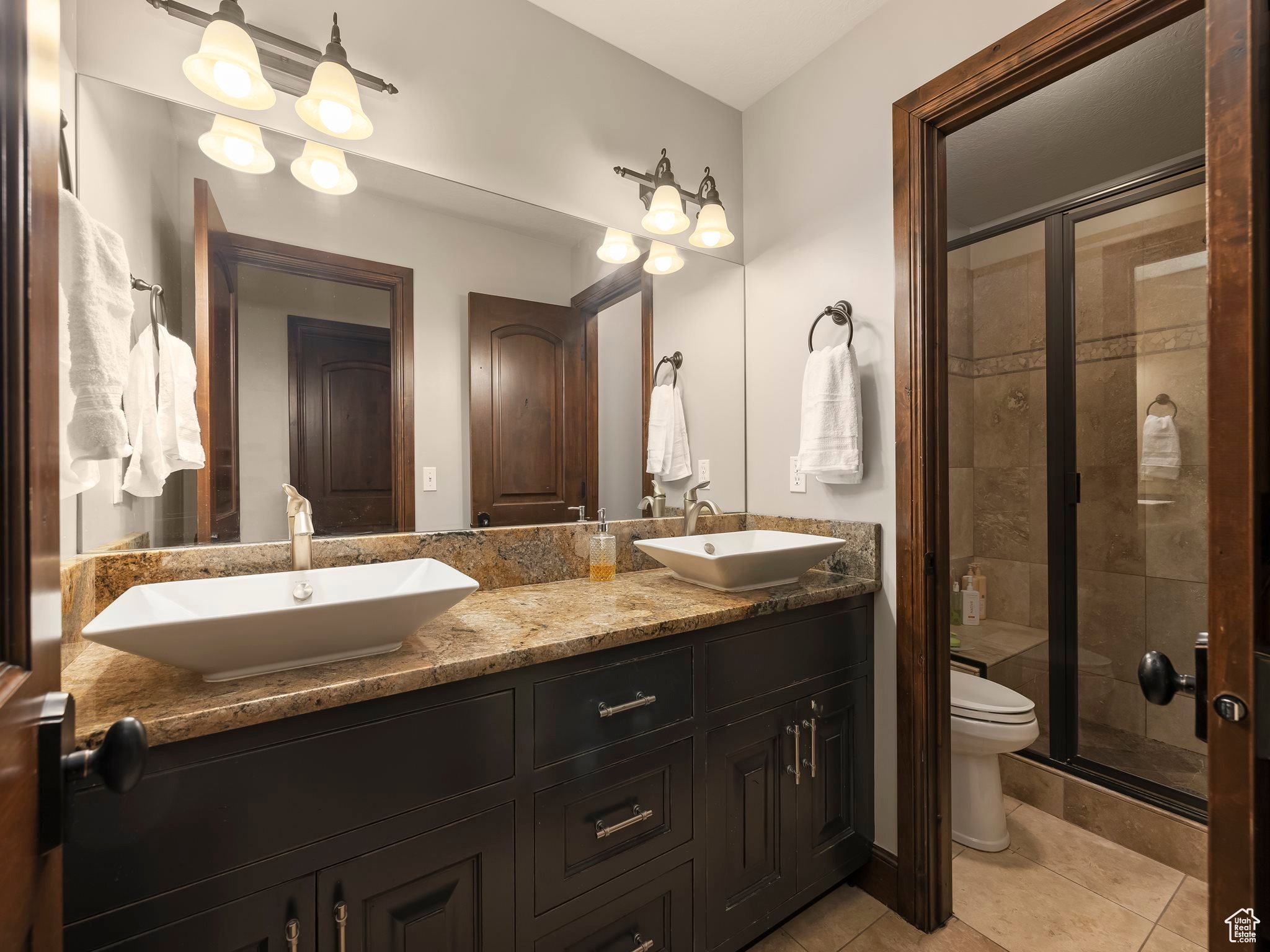 Dual vessel sinks set atop a stone countertop with dark wood cabinetry