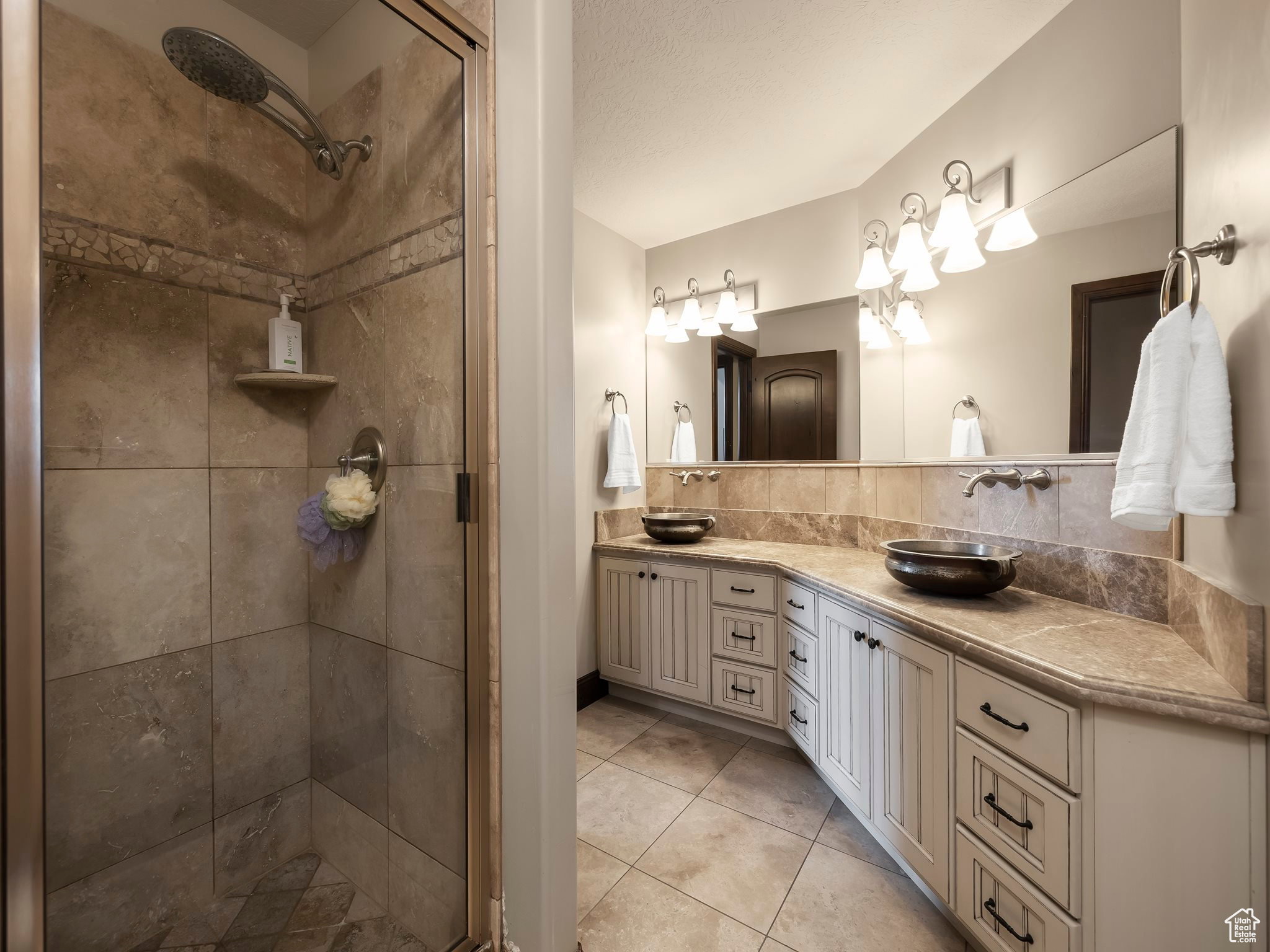 Dual vanity with vessel sinks, extensive countertop space, wood-finish cabinetry, and a full-width mirror