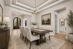 Tray ceiling with crown molding, light wood-finish flooring, stone accent walls, arched iron-forged entry doors, and a brass chandelier