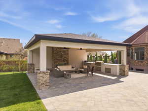 Covered outdoor living space featuring an integrated outdoor kitchen, brick accent wall, built-in ceiling fans, and a spacious paver patio