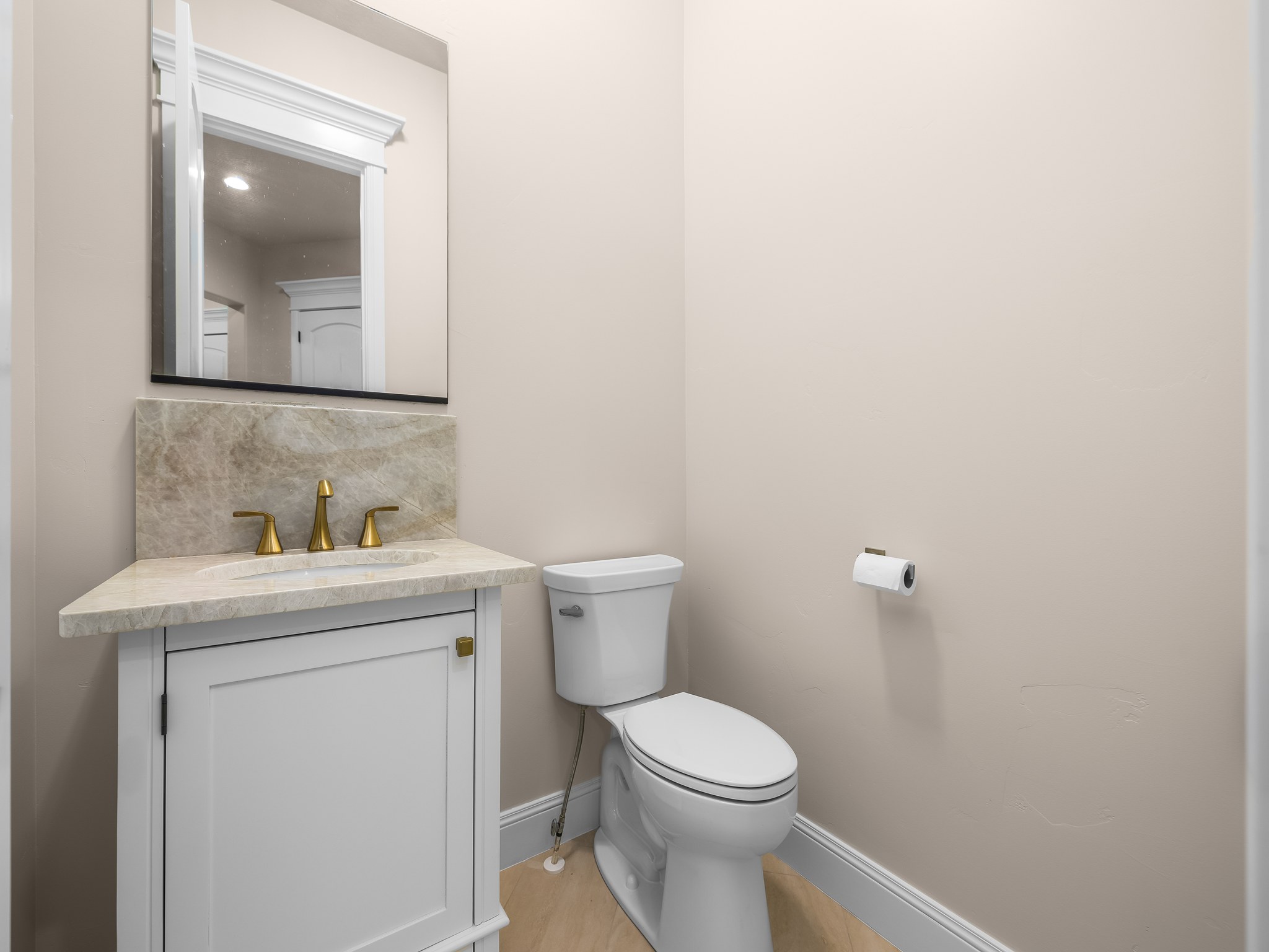 Powder room featuring a white single vanity with a light-toned stone countertop, matching stone backsplash, and brass-finish faucet