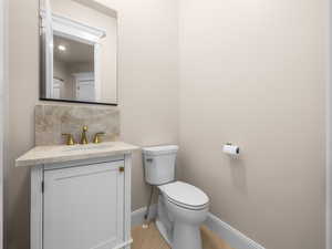 Powder room featuring a white single vanity with a light-toned stone countertop, matching stone backsplash, and brass-finish faucet