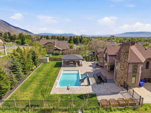Expansive backyard featuring a rectangular swimming pool, an adjacent covered outdoor living area, a stone paver patio, a multi-level composite deck, and a stone and stucco exterior