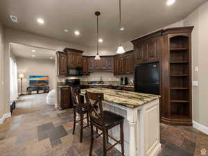 Apartment Kitchen featuring wood cabinetry, granite countertops, an integrated black appliance suite, a central island with breakfast bar, and slate-style flooring