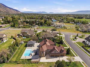 Stone and stucco exterior residence featuring a multi-car garage, pitched shingle roof, expansive paved driveway, and an in-ground swimming pool with an adjacent covered patio structure
