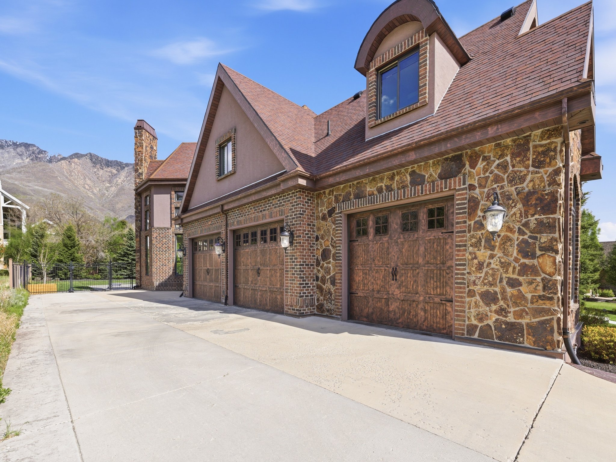 Three-car garage featuring custom wood-finish doors with decorative hardware, stone and brick exterior, and a dormer window