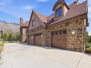 Three-car garage featuring custom wood-finish doors with decorative hardware, stone and brick exterior, and a dormer window