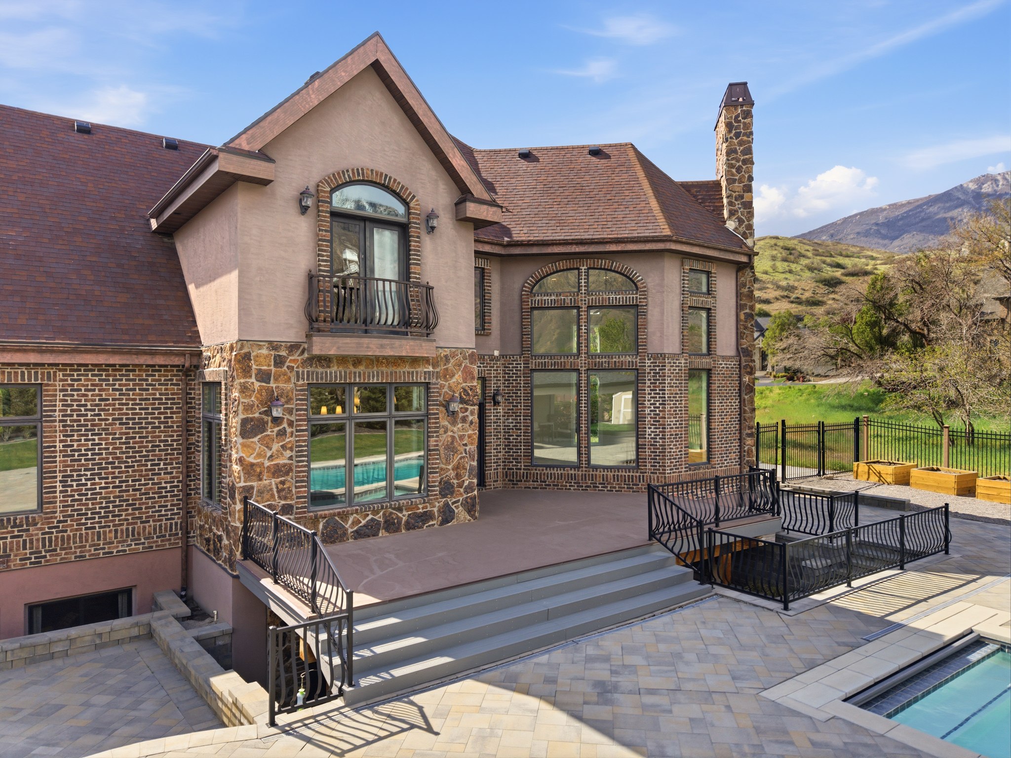 Multi-level exterior featuring brick and stone veneer, a large deck with steps, a paver patio, an in-ground swimming pool, and a stone chimney
