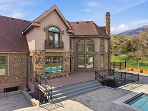Multi-level exterior featuring brick and stone veneer, a large deck with steps, a paver patio, an in-ground swimming pool, and a stone chimney