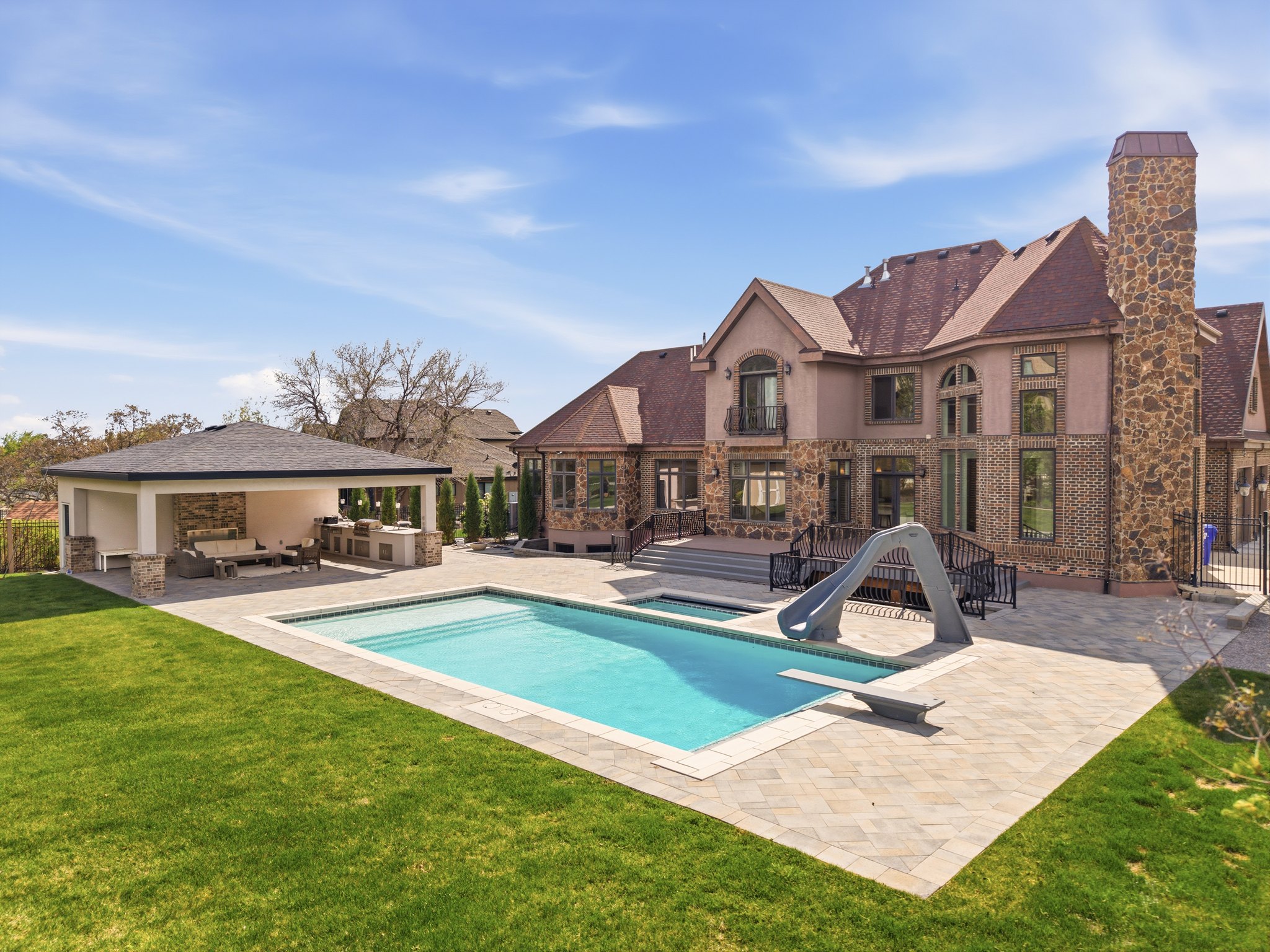 Expansive backyard oasis featuring a rectangular swimming pool with integrated slide and diving board, surrounded by paver decking