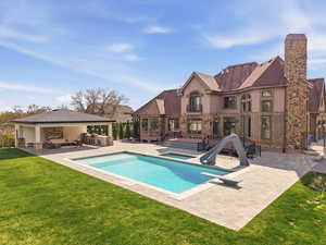 Expansive backyard oasis featuring a rectangular swimming pool with integrated slide and diving board, surrounded by paver decking