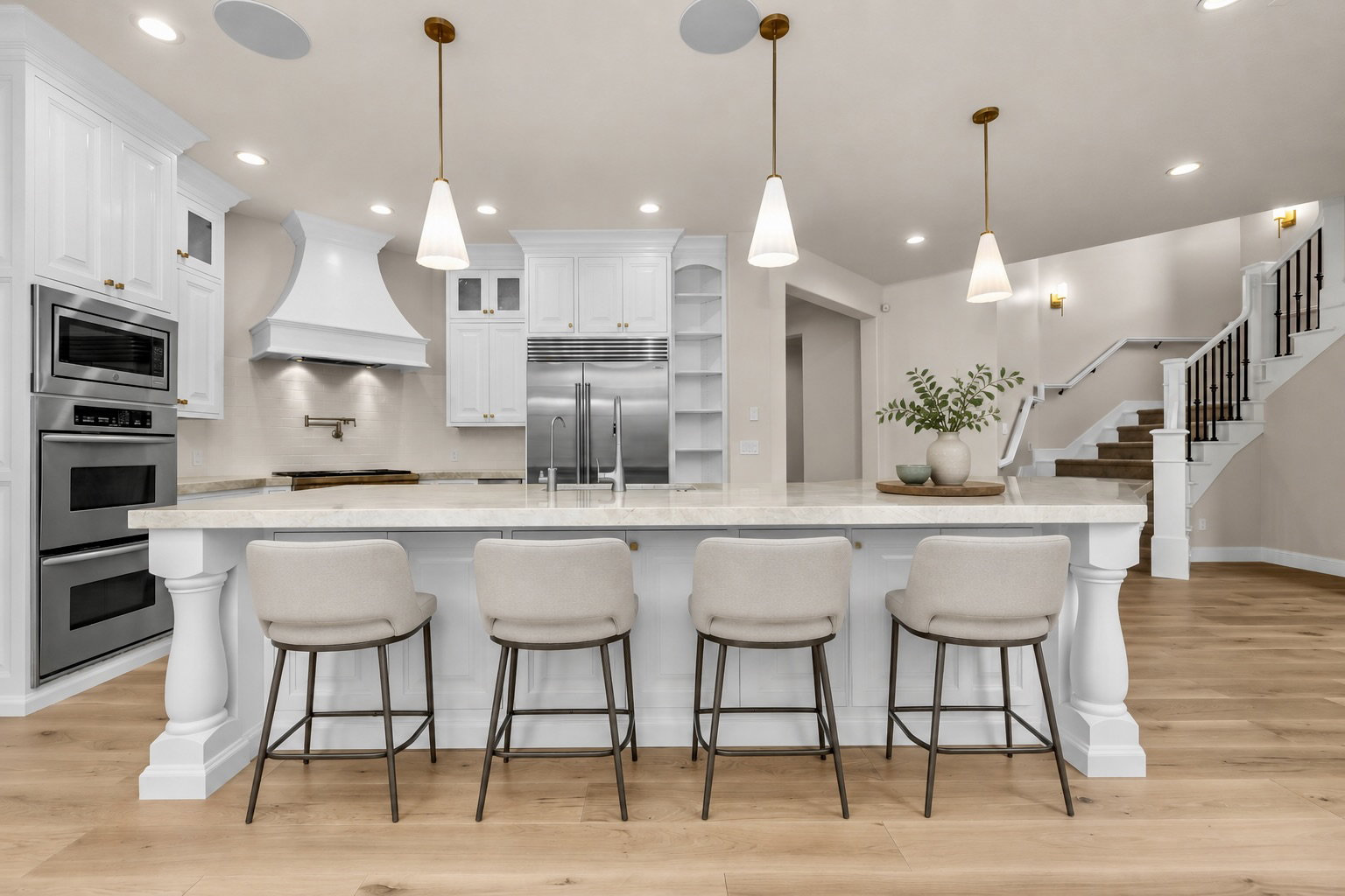 Gourmet kitchen with an expansive island featuring decorative balusters and pendant lighting, white cabinetry, stainless steel double ovens, and a built-in refrigerator