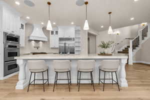 Gourmet kitchen with an expansive island featuring decorative balusters and pendant lighting, white cabinetry, stainless steel double ovens, and a built-in refrigerator