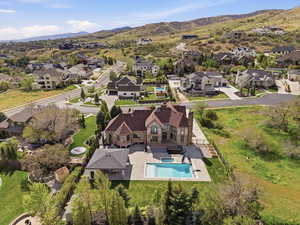 Stone and stucco exterior with a multi-level roofline, featuring an expansive backyard with an in-ground swimming pool, an adjacent covered patio area, and mature landscaping