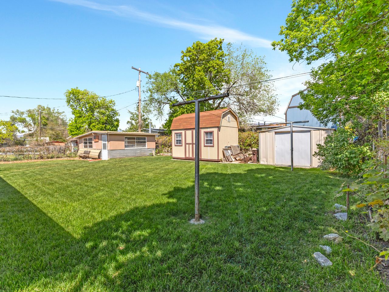 Expansive green lawn featuring a brown shed with white trim and a metal storage shed