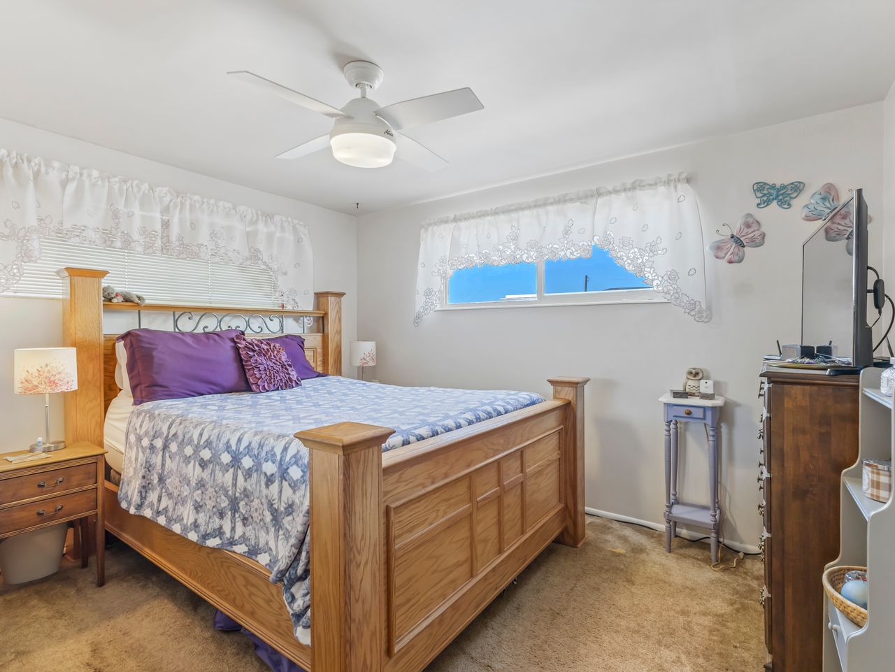 Bedroom featuring light-toned walls, a white ceiling fan with integrated lighting, two windows with horizontal blinds, and carpeting