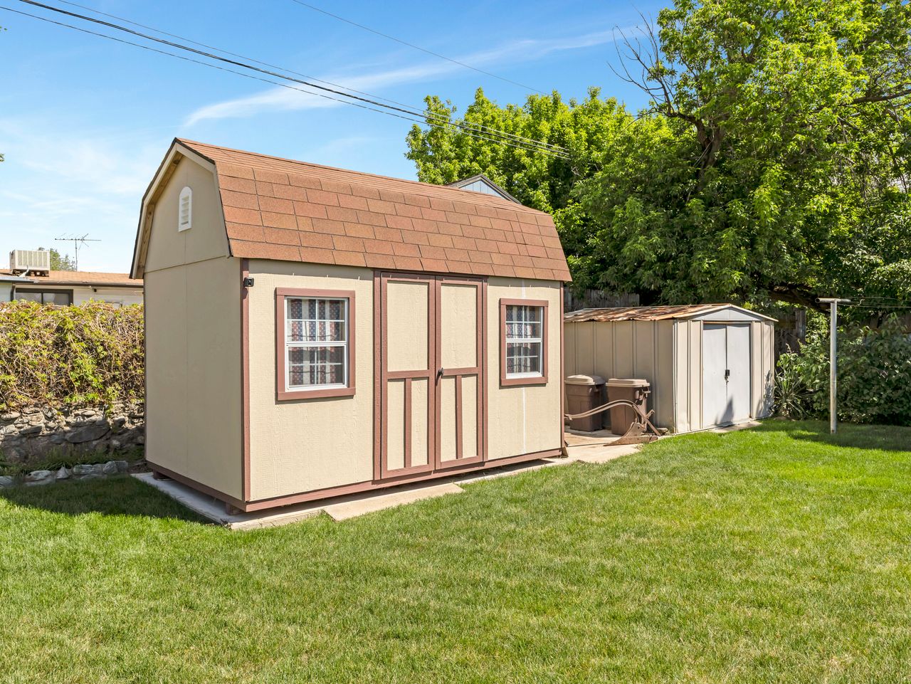 Spacious backyard featuring a gambrel-roof storage shed with dual double doors and two windows, a secondary metal storage shed, and a verdant lawn