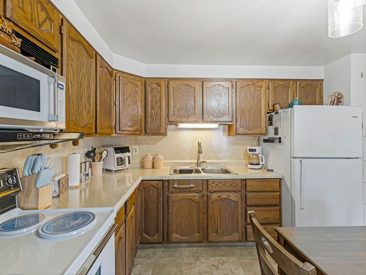 Kitchen featuring wood cabinetry, solid surface countertops, double basin sink with gooseneck faucet, built-in microwave, and white appliances