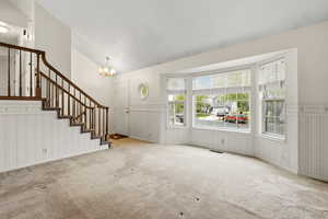 Spacious living area featuring a prominent staircase with wood railings, a large bay window, and a front entry door with an overhead light fixture