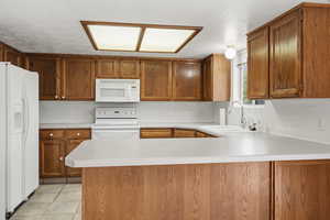 Kitchen featuring wood cabinetry, white appliances, light-toned countertops.