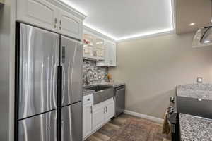 Modern kitchen featuring a stainless steel French door refrigerator, white cabinetry, a farmhouse sink, stone countertops, and a subway tile backsplash