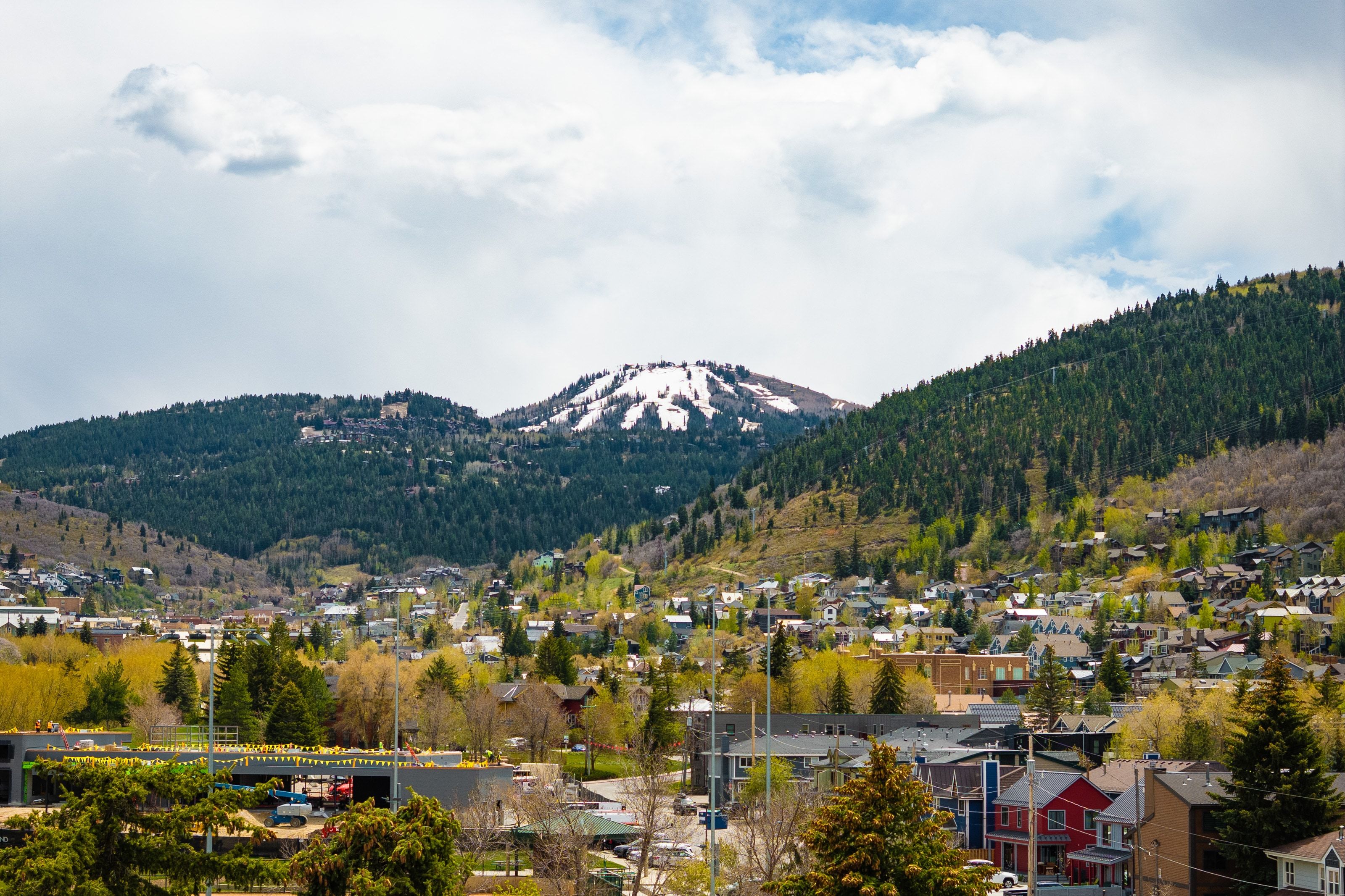 Mountainous landscape featuring a snow-capped peak, dense evergreen forests, and a scattering of residential structures
