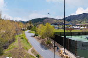 Paved pathway bordered by green spaces, leading towards a mountainous backdrop with snow-capped peaks