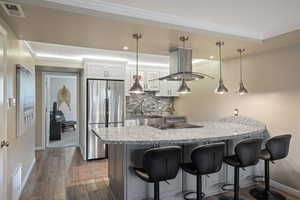 Kitchen featuring a granite-topped island with seating, stainless steel appliances, a tiled backsplash, and recessed and pendant lighting