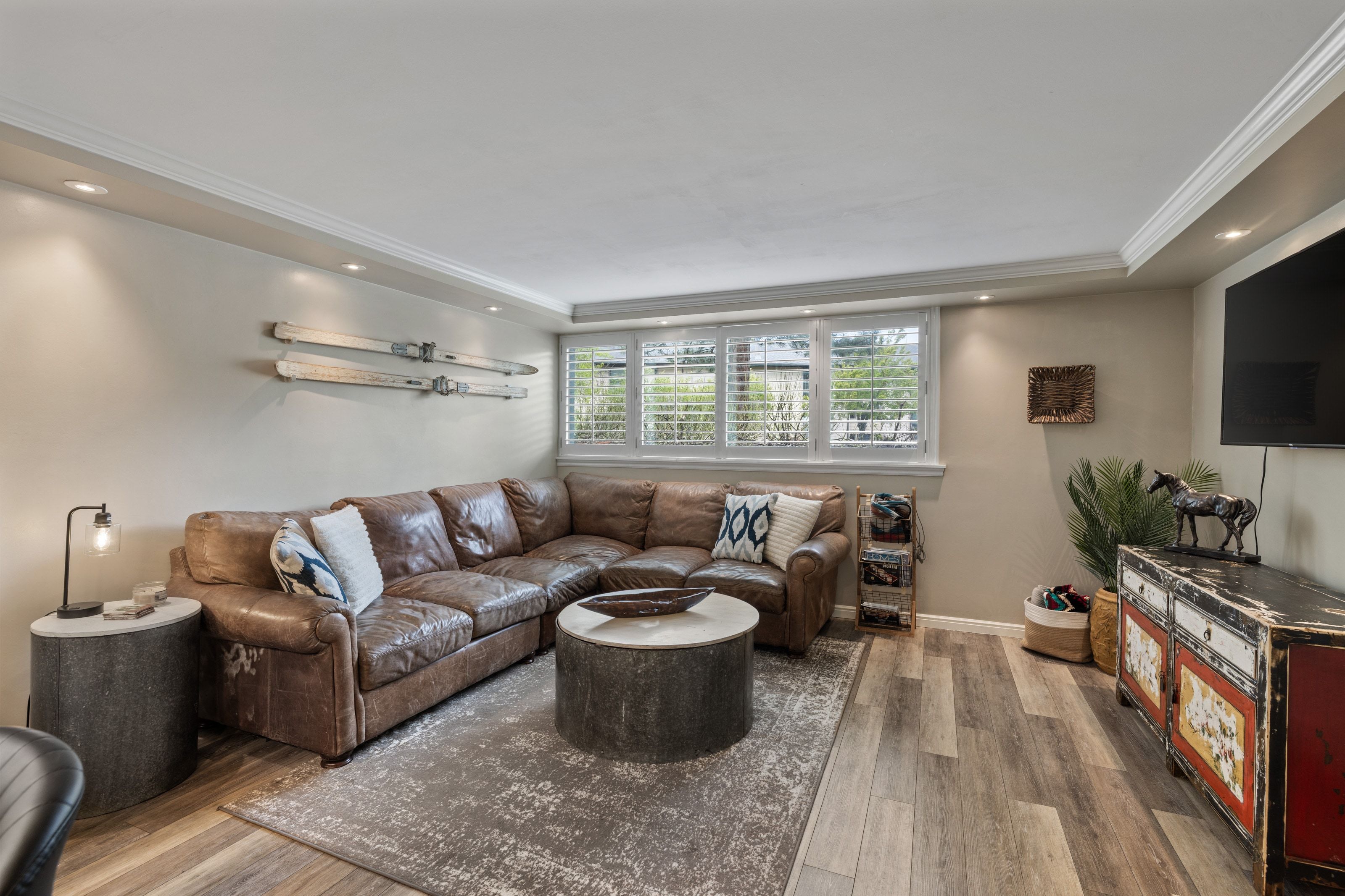 Living area featuring wood-finish flooring, recessed lighting, crown molding, and a window with plantation shutters
