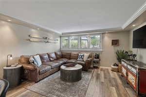 Living area featuring wood-finish flooring, recessed lighting, crown molding, and a window with plantation shutters