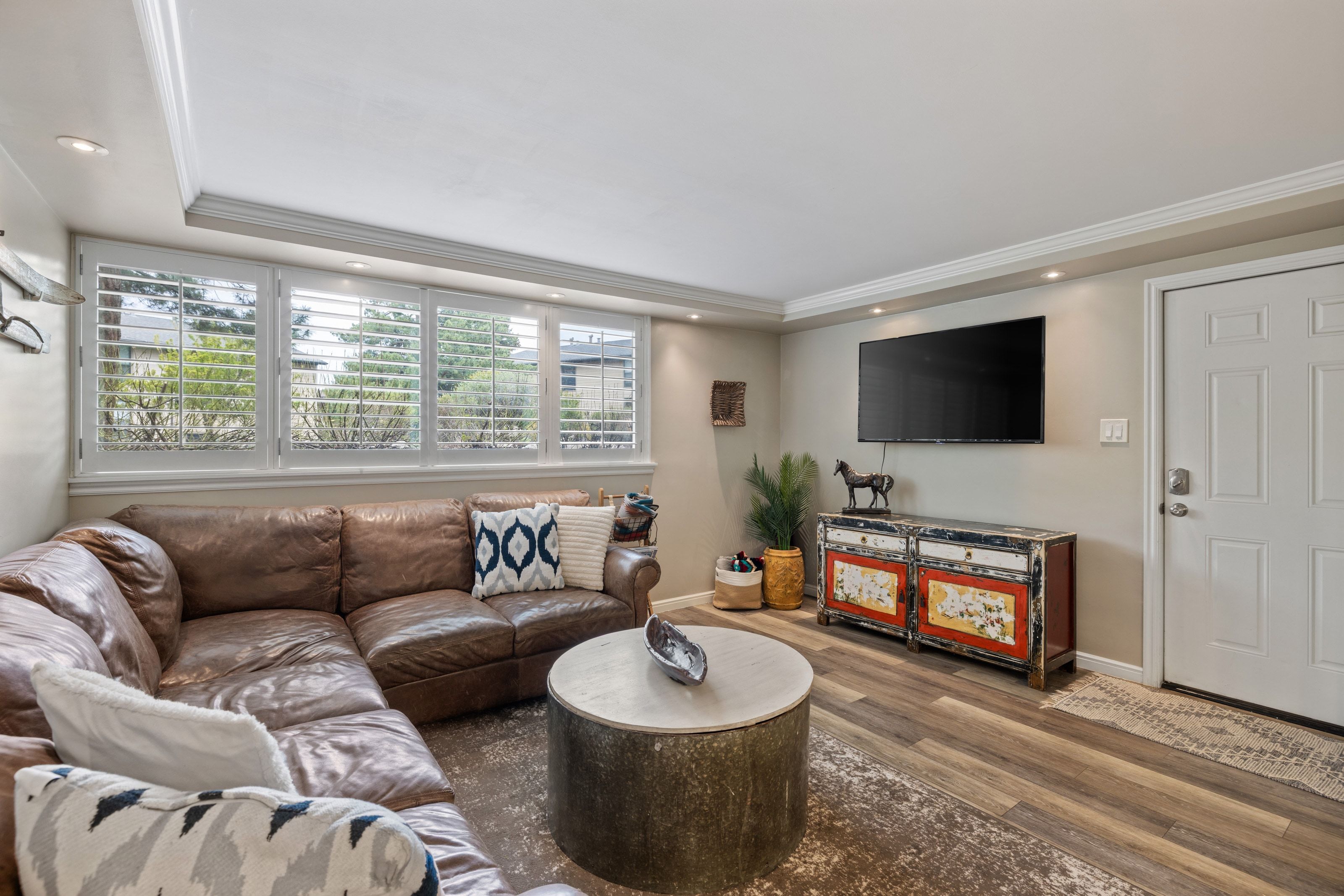 Recessed lighting illuminates this living space featuring a row of four windows with white plantation shutters, wood-finish flooring, and crown molding